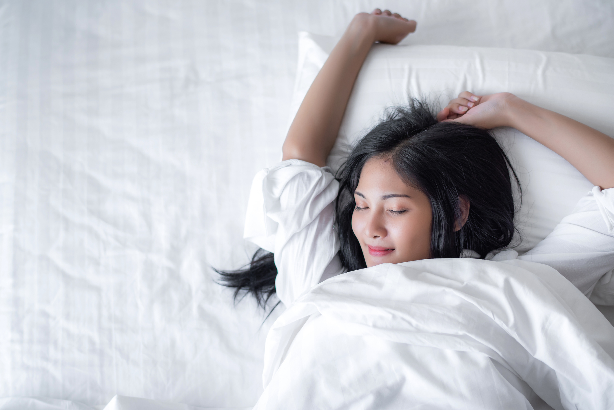 Beautiful young pretty Asian woman wake up and make happy smile with white shirt at the white bed in the morning. Beautiful young pretty Asian woman wake up and make happy smile with white shirt at the white bed in the morning.