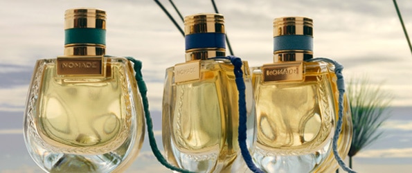 Tri zlaté flakóny parfumu Chloé Nomade Jardin d’Égypte vystavené na prírodnom pozadí oblohy.